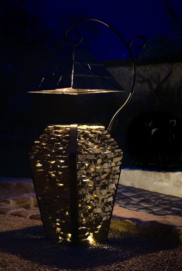Image montrant une lampe extérieur en pierres et aciers, sur une sublime allée en pavés entourée de murs de pierres intégrant des éclairages.