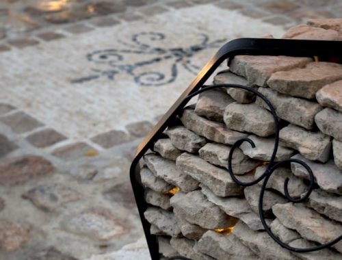 Image montrant une partie d'un luminaire extérieur en pierres et aciers, sur une sublime allée en pavés entouré de murs de pierre intégrant des éclairages.