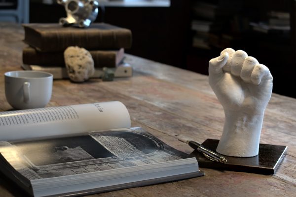 sculpture d'une main en plâtre blanc et son socle en acier posée sur une table