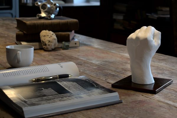 sculpture d'une main en plâtre blanc et son socle en acier posée sur une table