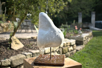 sculpture d'un nez en béton blanc sur un socle en acier, arrosée par de l'eau