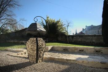 Image montrant une lampe extérieur en pierres et acier avec un abat jour en ardoises dans un jardin avec une allée en pavés.