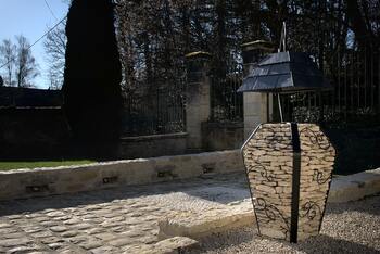 Image montrant une lampe extérieur en pierres et acier avec un abat jour en ardoises dans un jardin avec une allée en pavés.